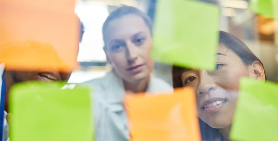 Junge Personen, die auf Post-its an einer Glaswand schreiben.