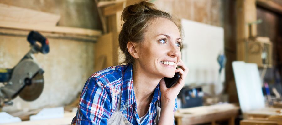 Eine Frau telefoniert vorgebeugt über einer Holzwerkbank.