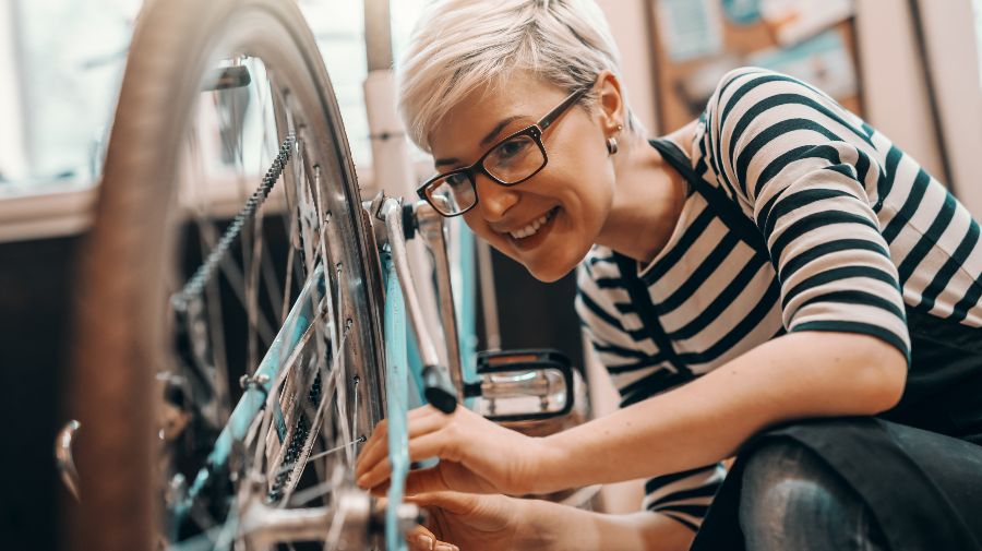 Eine Frau begutachtet den hinteren Reifen eines Fahrrads, welches auf dem Lenker steht. 