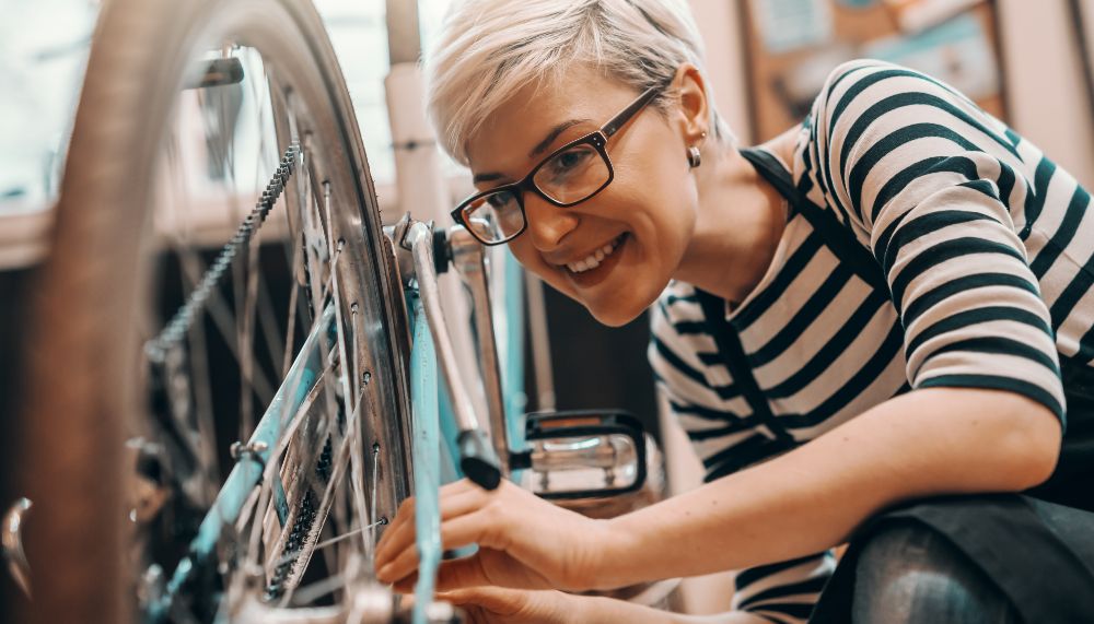 Eine Frau begutachtet den hinteren Reifen eines Fahrrads, welches auf dem Lenker steht.
