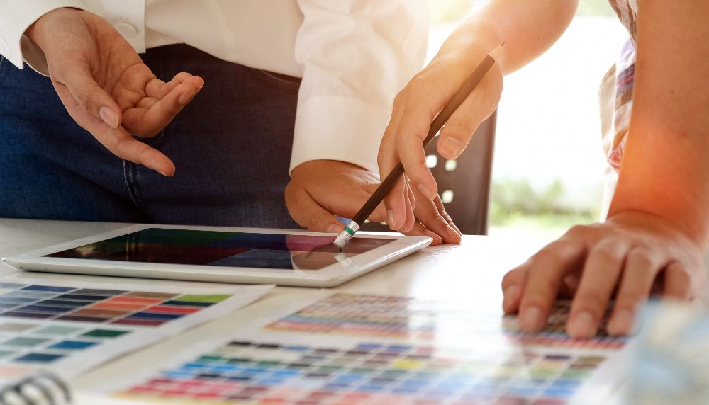 Four hands belonging to two people can be seen gesturing towards a map and a tablet on a table.