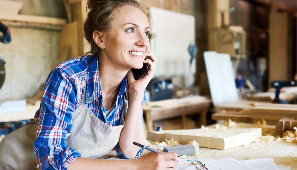 A woman is on the phone, leaning over a wooden workbench.