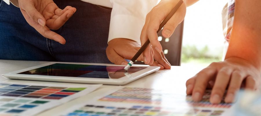  Four hands belonging to two people can be seen gesturing towards a map and a tablet on a table.
