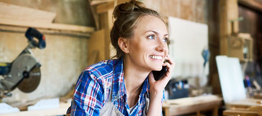 A woman is on the phone, leaning over a wooden workbench.