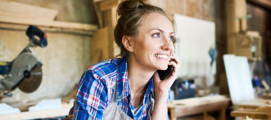  Une femme téléphone, penchée en avant au-dessus d'un établi en bois.
