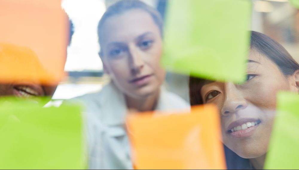  Des jeunes écrivant sur des Post-it collés sur une paroi vitrée.