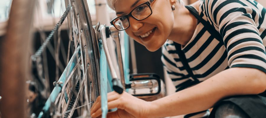 A woman is inspecting the rear tyre of a bicycle, which is propped up on its handlebars. 