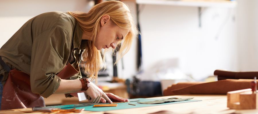 A young woman is cutting a piece of leather in a workshop.