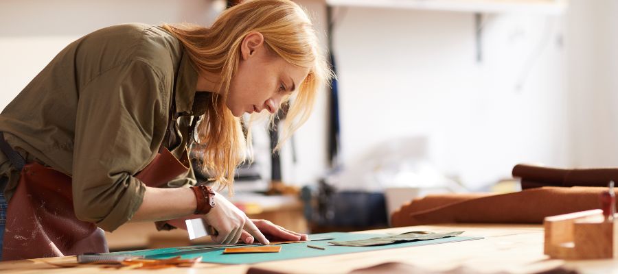 Une jeune femme découpe un morceau de cuir dans un atelier.