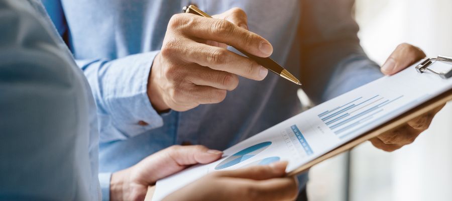 A close-up of two pairs of hands holding a clipboard with a diagram on it. One hand is pointing at the diagram with a pen.