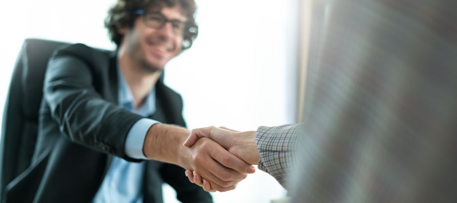 A young man wearing glasses is shaking hands with someone who is not visible in the picture.