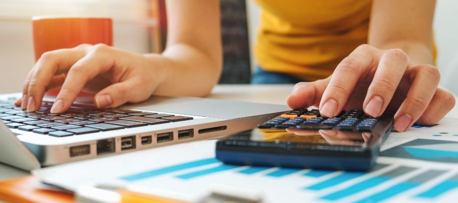 A person is typing on a laptop and a calculator at the same time.
