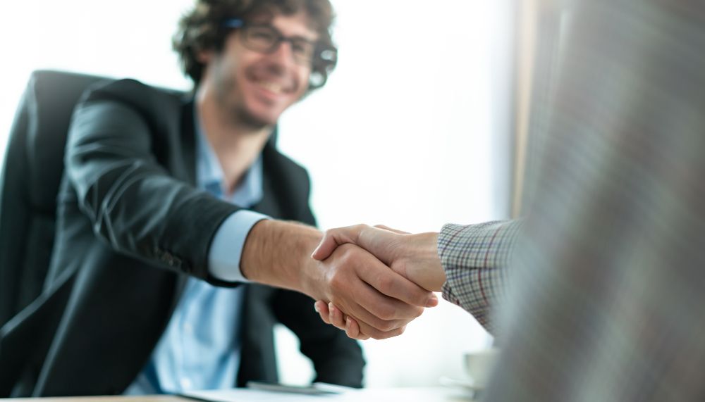 Un jeune homme à lunettes tend la main à une personne qui n'apparaît pas sur la photo.