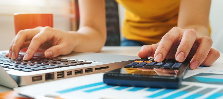 Une personne tape à la fois sur un ordinateur portable et sur une calculatrice.