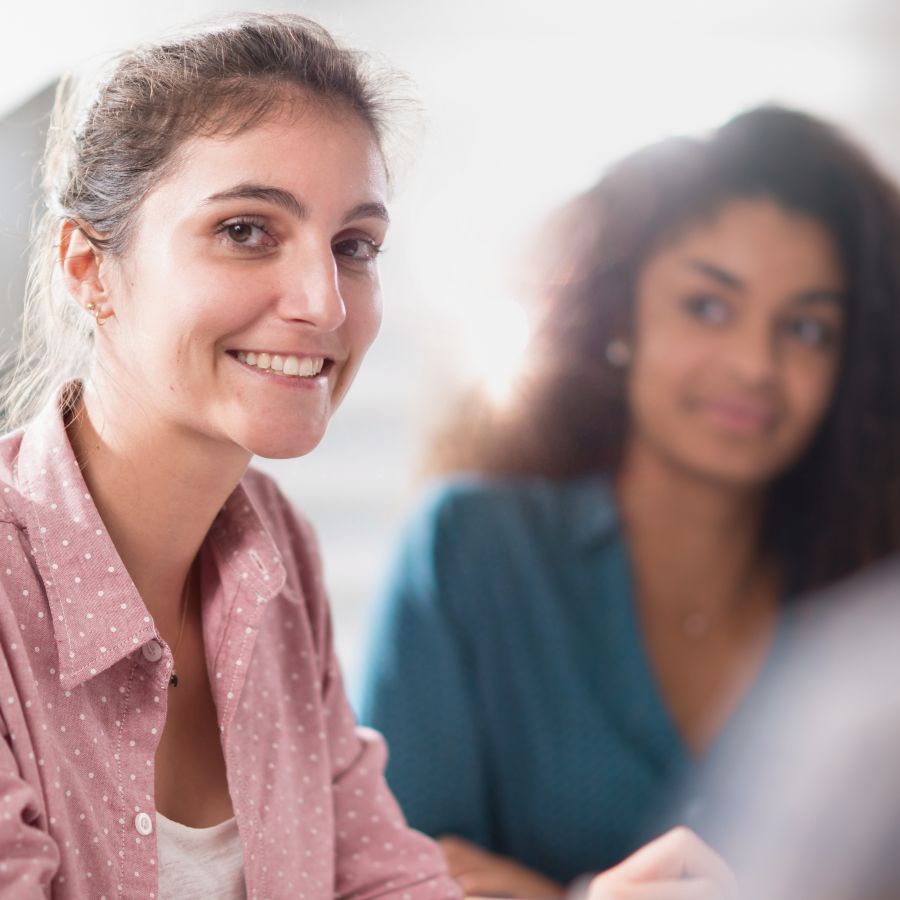 A young woman wearing a blue blouse with white vertical stripes smiles at the viewer during a meeting. 