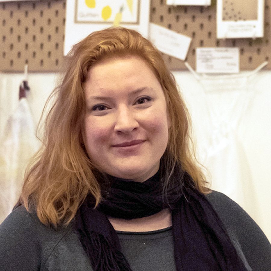 A young woman with reddish-blonde hair and a black scarf smiles at the viewer.