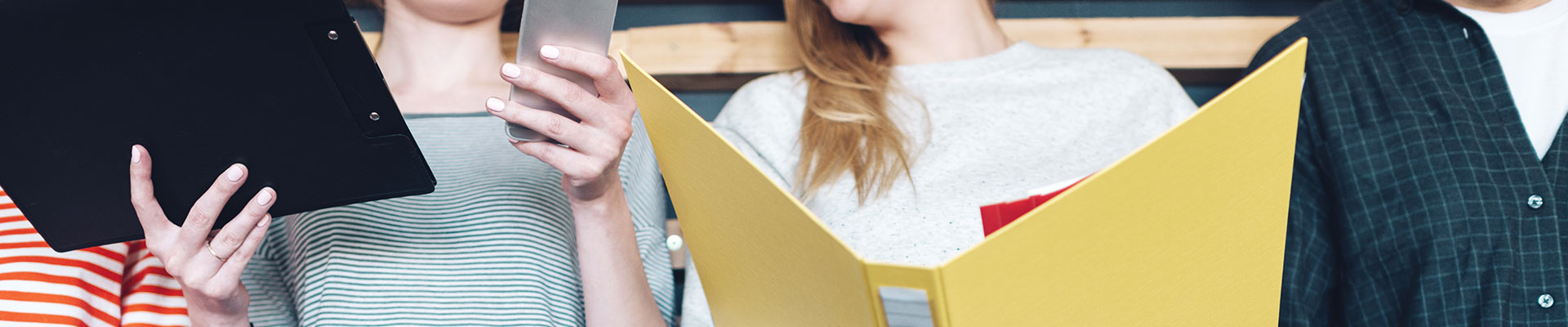 Close-up of women with clipboard, smartphone and folder.