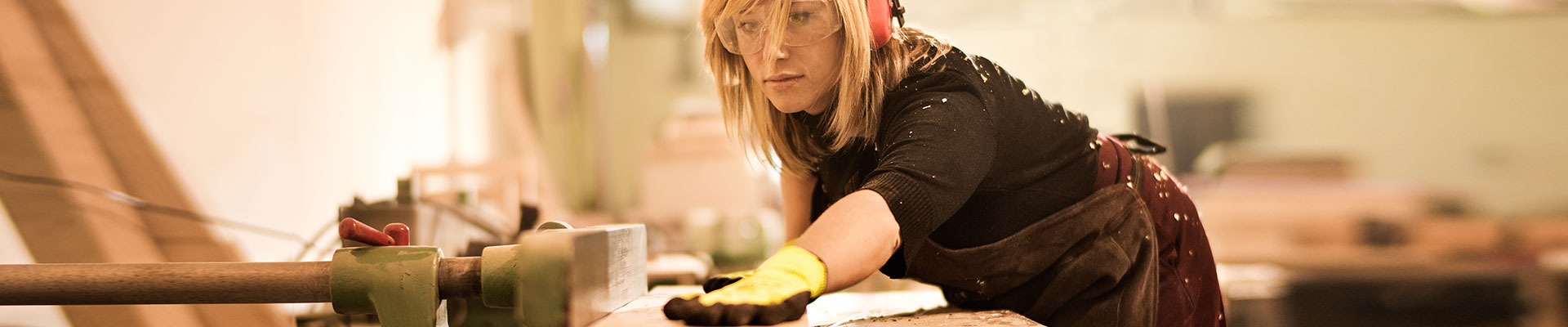 A woman wearing protective goggles and protective gloves works at a workbench.