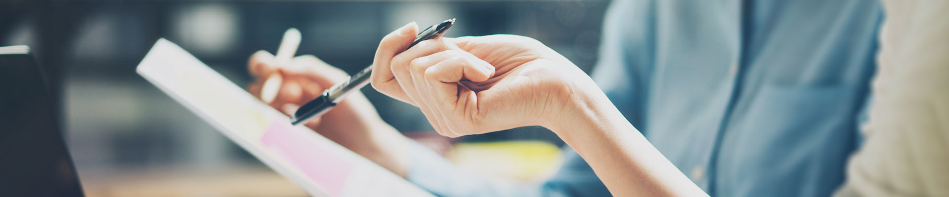 A hand shows at a piece of paper with a pen.