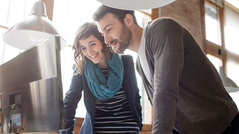 A young woman and a young man look at a screen. 