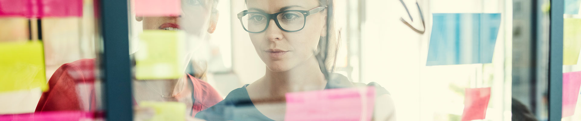 Two women look at post-its on a wall.