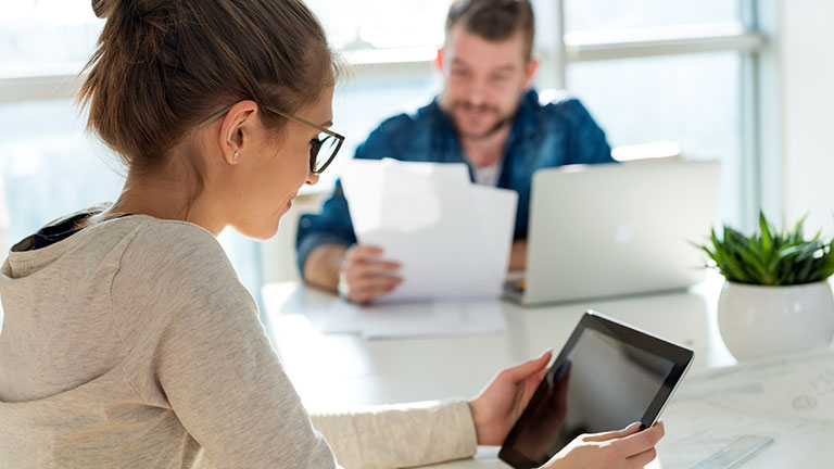 Eine Frau und im Hintergrund ein Mann lesen in Unterlagen.