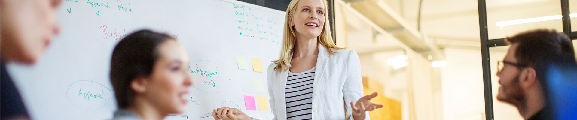 A woman stands in front of a whiteboard and gives a presentation.