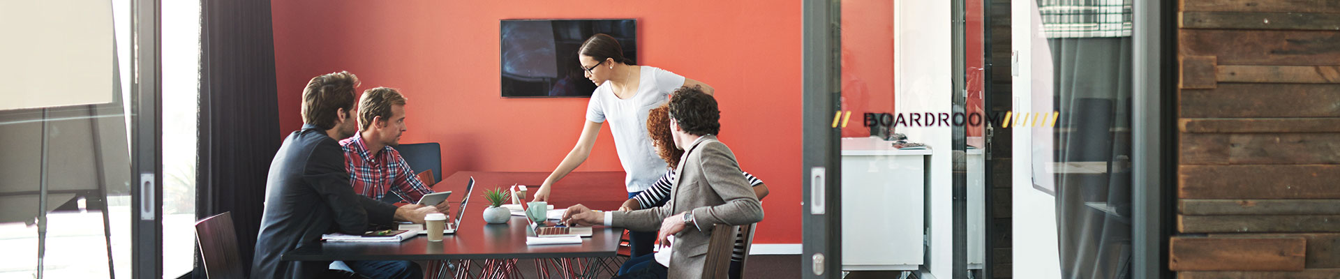 A group of men and women are working with laptops and tablets on a big desk.