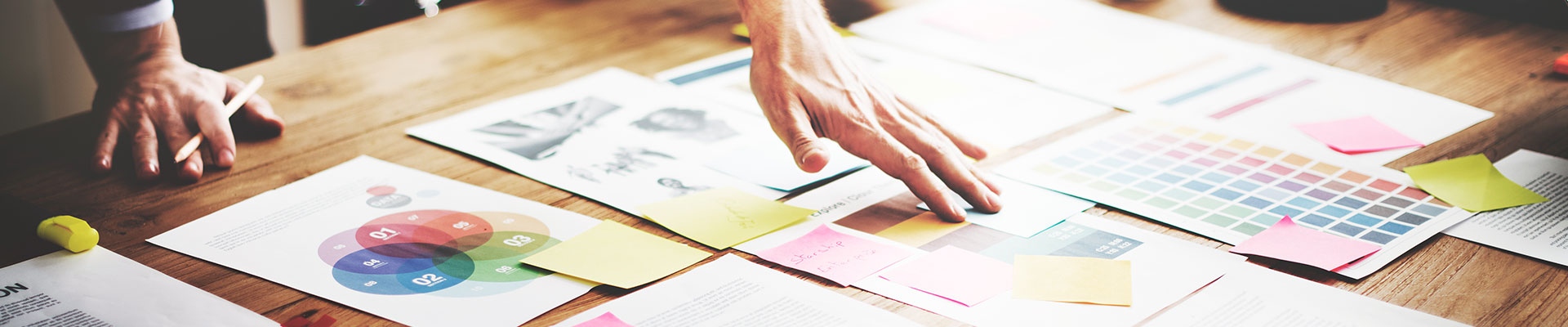 A hand arranges notes with texts and graphics on a wooden table.