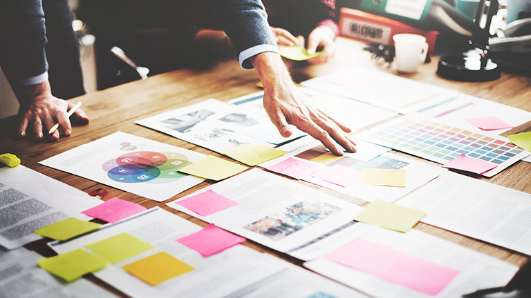 Une main organise des notes avec textes et graphiques sur une table en bois.