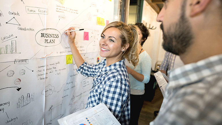 A woman creates a business plan on a metaplan wall.