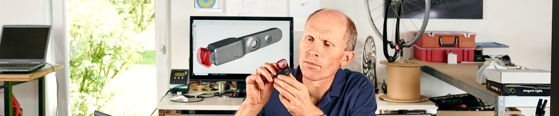 Dirk Strothmann sits in repair shop at desk, works in front of a laptop.