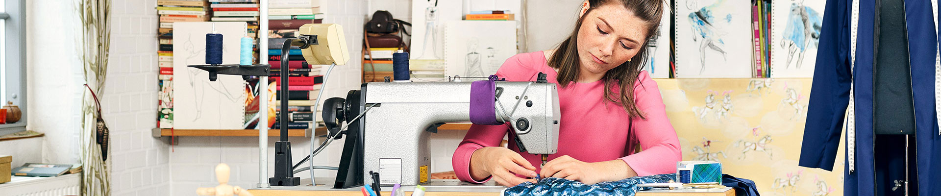 Eine junge Frau näht in einem Atelier an einer Nähmaschine.
