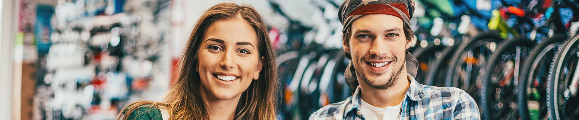 Jeune femme et jeune homme dans un magasin de bicyclettes, sourient à la caméra.