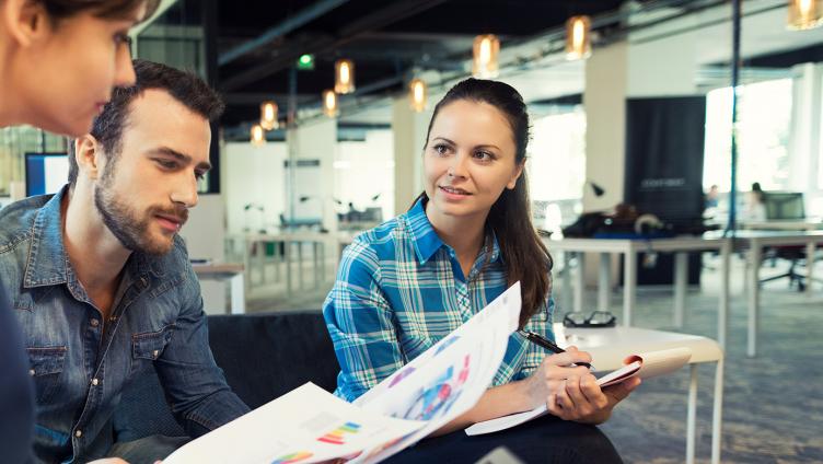 Two women and men sit together and look at documents. 