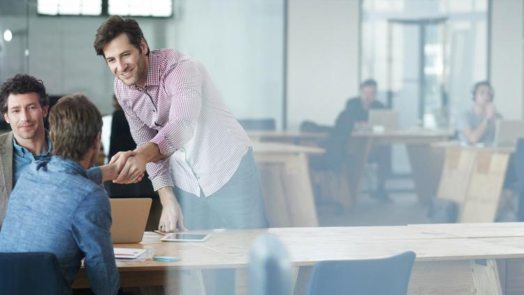 Two men shake hand over a table. 