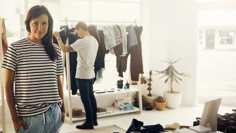 A young woman with her hands in her pockets is standing in a boutique.