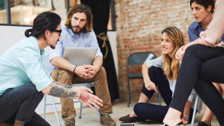 A group of young women and men sit together and talk.