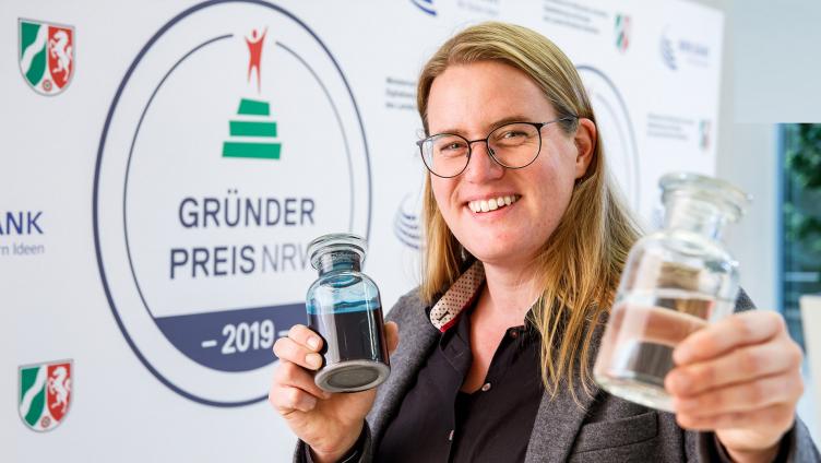 Eine Frau mit Brille hält lächelnd zwei Glasflaschen in den Händen.