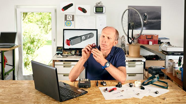 Dirk Strothmann sitzt in einer Werkstatt an einem Schreibtisch und arbeitet an einem Laptop.